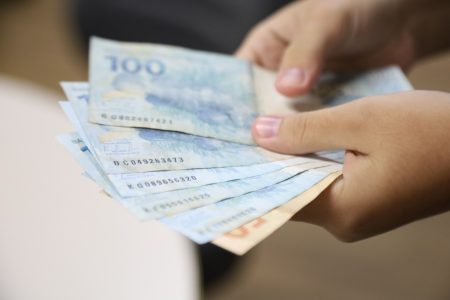 Mãos seguram cédulas de 100 e 50 reais