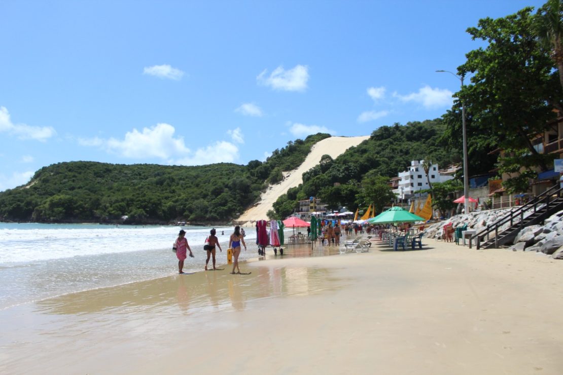 Banhistas andam na areia da praia com Morro do Careca ao fundo