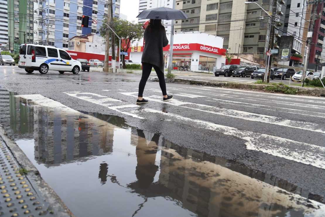 Mulher segura guarda chuvas enquanto atravessa faixa de pedestre