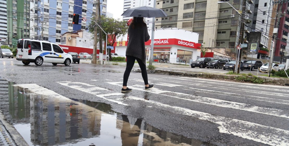 Mulher segura guarda chuvas enquanto atravessa faixa de pedestre