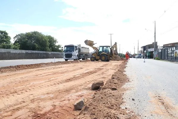 Estrada em obras com caminhão e máquina trabalhando ao fundo